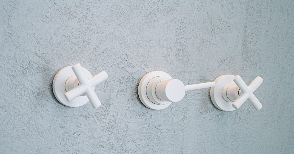Waterproof wall plaster surface in Terrazzo GraniTech finish with textured gray appearance, featuring three modern white bathroom fixtures mounted on the wall